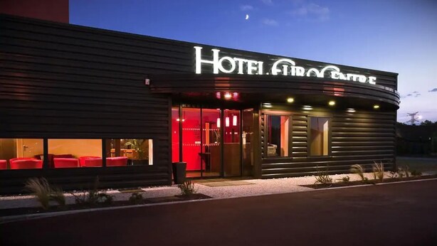 A modern hotel with a curved facade, large glass entrance, and red seating area outside. - Hôtel Eurocentre Toulouse Nord 2 Stars (Castelnau-d'Estretefonds)