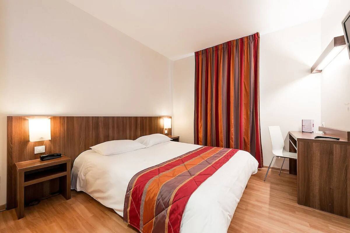 Quarto de hotel com cama, mesas de cabeceira, escrivaninha e uma cadeira.