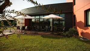 A modern building with a patio area featuring outdoor seating and umbrellas. - Hôtel Eurocentre Toulouse Nord 2 Stars (Castelnau-d'Estretefonds)
