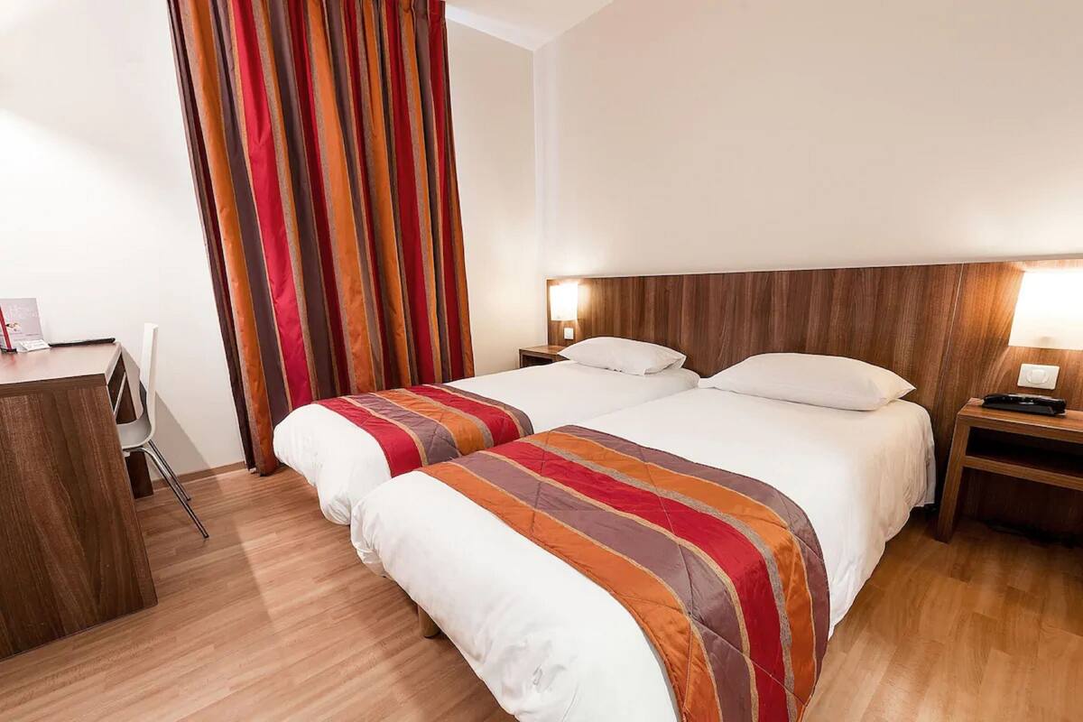 Quarto de hotel com duas camas, uma escrivaninha e uma cadeira.