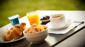 Un desayuno con croissants, un tazón de cereal, un vaso de jugo de naranja y una taza de café en una mesa al aire libre.