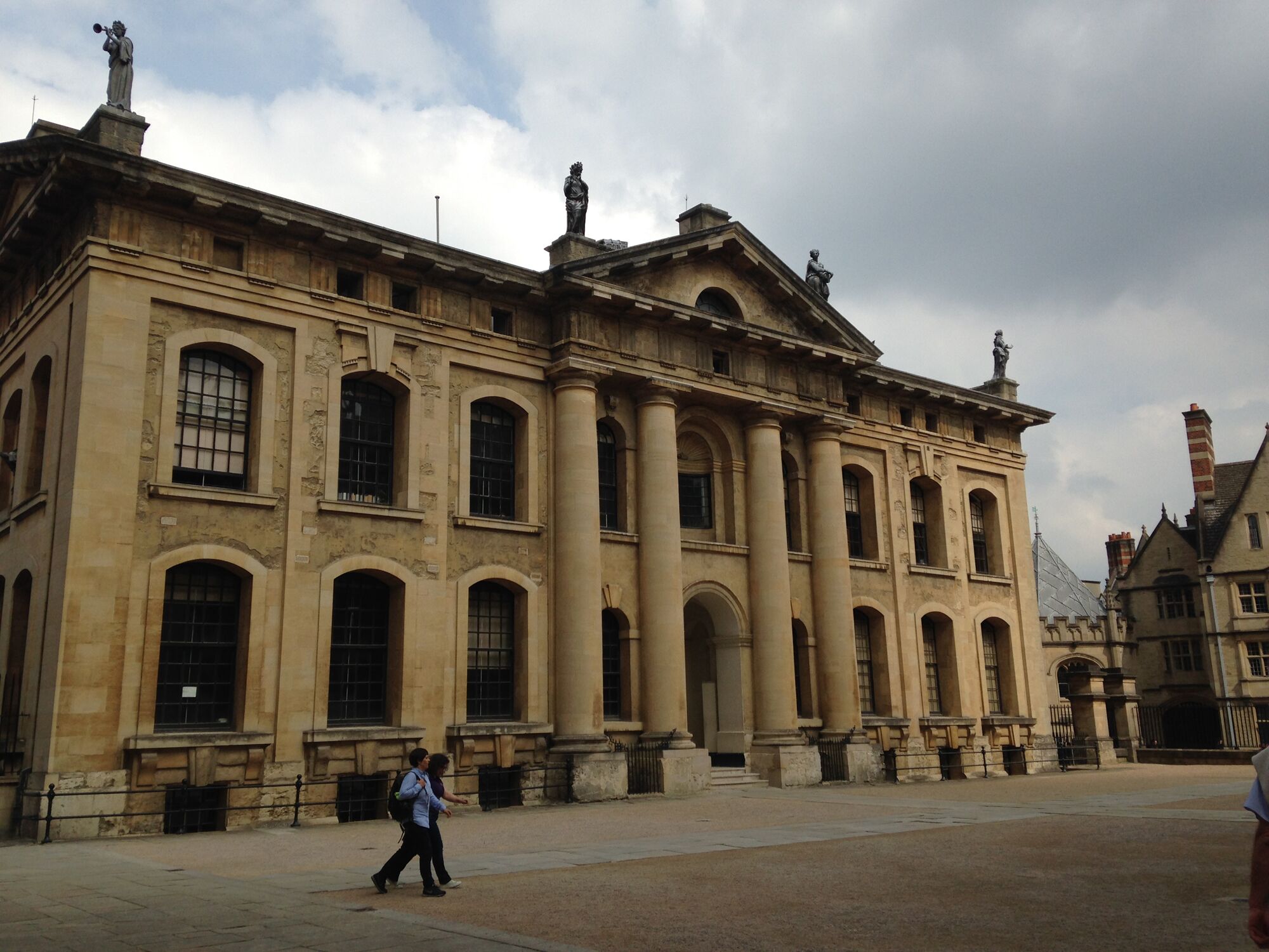 A historic building with classical architecture, featuring large columns and statues on the roof.