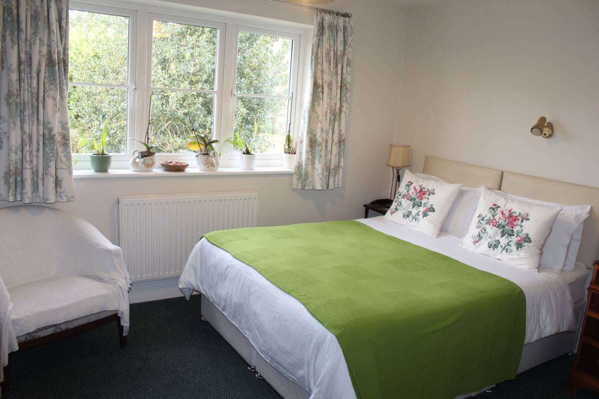 A bedroom with a large bed, a chair, a window with curtains, and a radiator.