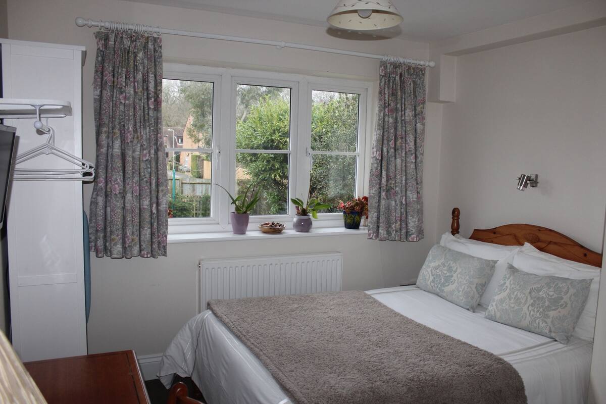 A bedroom with a bed, a window with curtains, a radiator, and a wooden headboard.