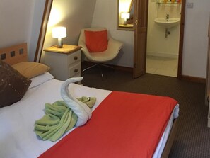 Een hotelkamer met een bed, een stoel, een nachtkastje, een lamp en een badkamer zichtbaar door een geopende deur.