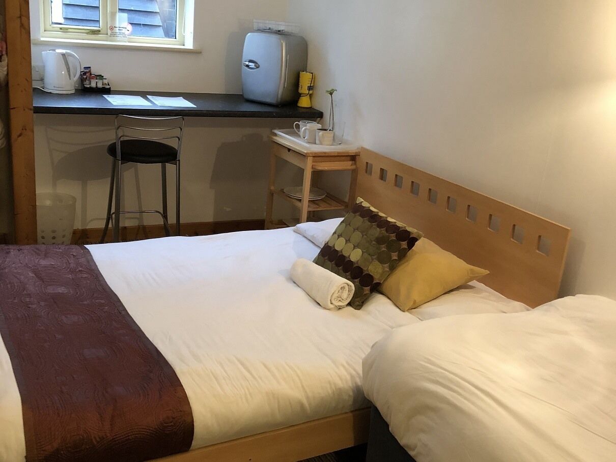 A double bed with a wooden headboard, a small table with a kettle and a toaster, and a chair.