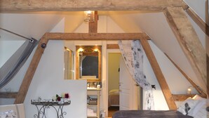 A bedroom with a sloped ceiling, a bed, a small table with flowers, and a mirror. - Maison D'hôtes La Bihorée (Saint-Jean-de-Livet)