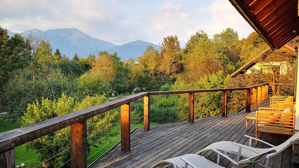 A wooden deck with two white chairs and a table, overlooking a forested area with mountains in the distance.