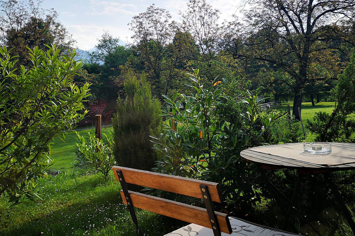 A wooden bench and table set in a lush garden with a view of a distant mountain range.