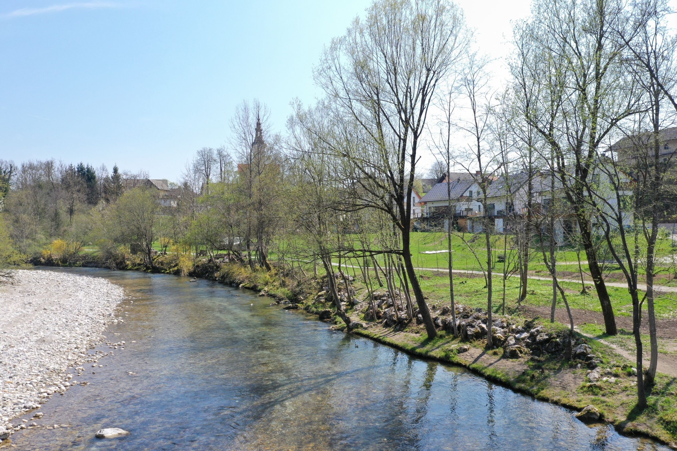 Un río de aguas cristalinas, rodeado de árboles y un muro de piedra.