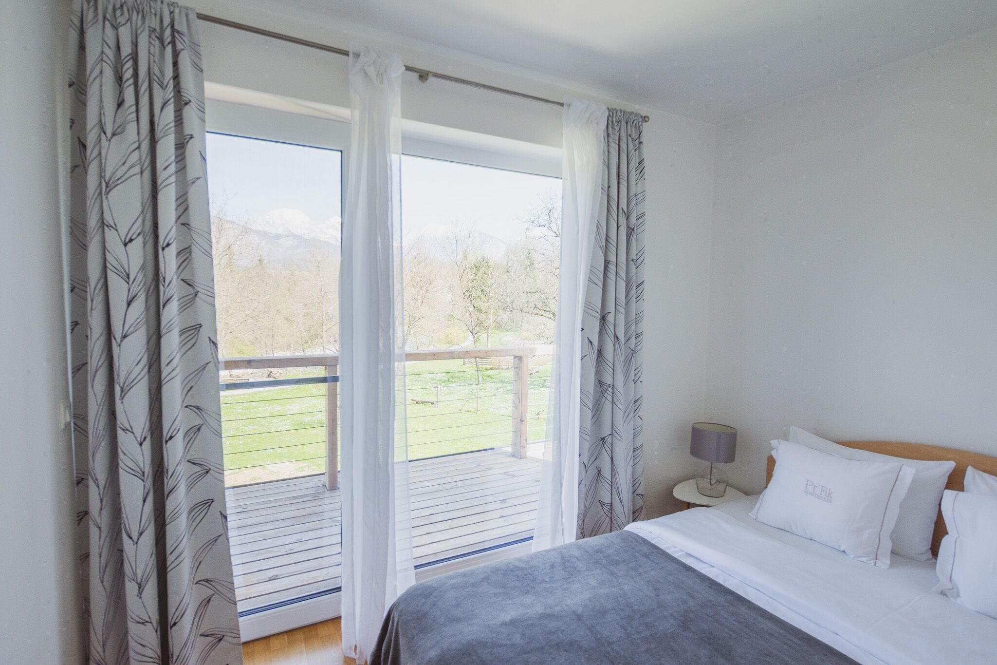Ein Schlafzimmer mit großem Fenster, einem Bett mit weißer Bettwäsche und einem Nachttisch mit Lampe.