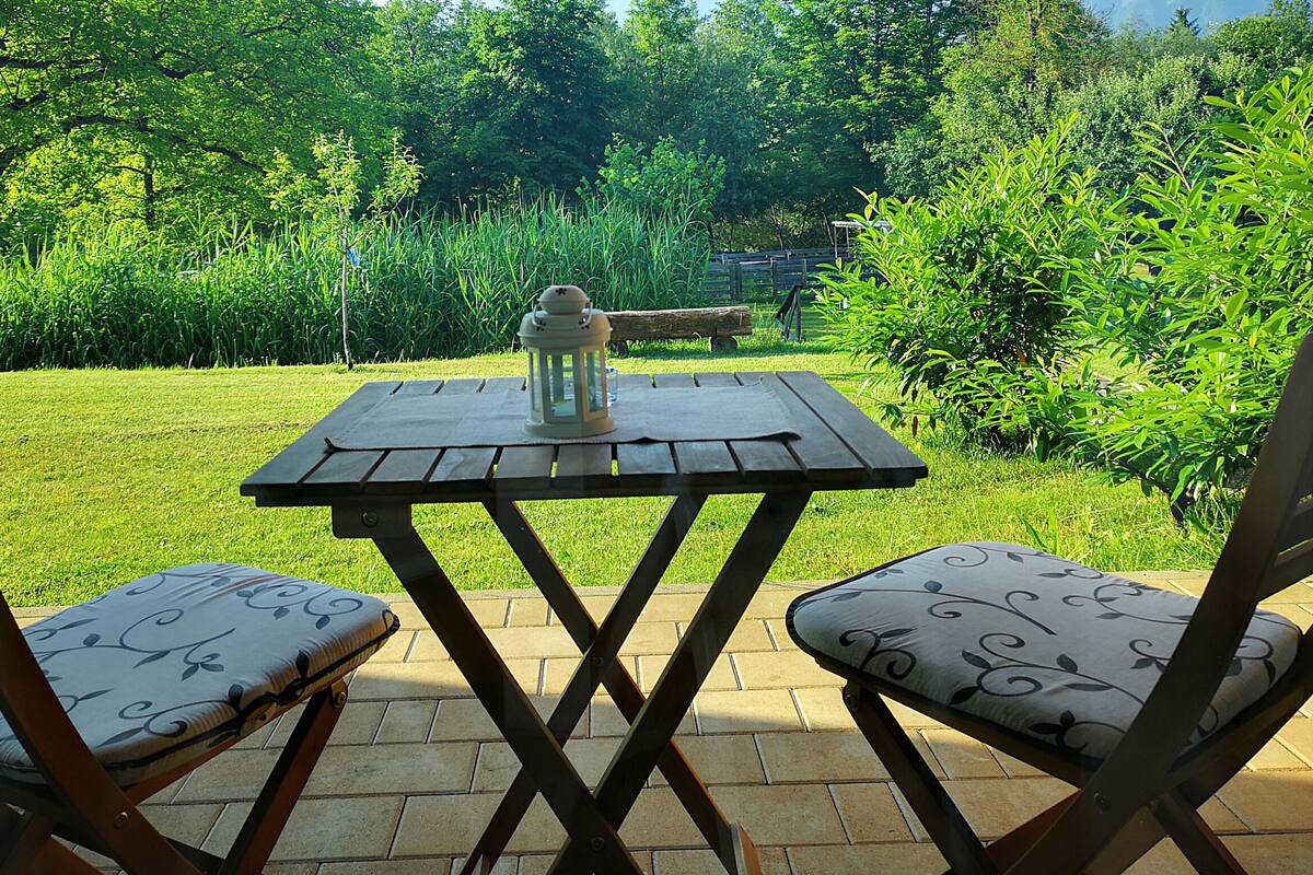 A patio with a table and two chairs, surrounded by lush greenery.