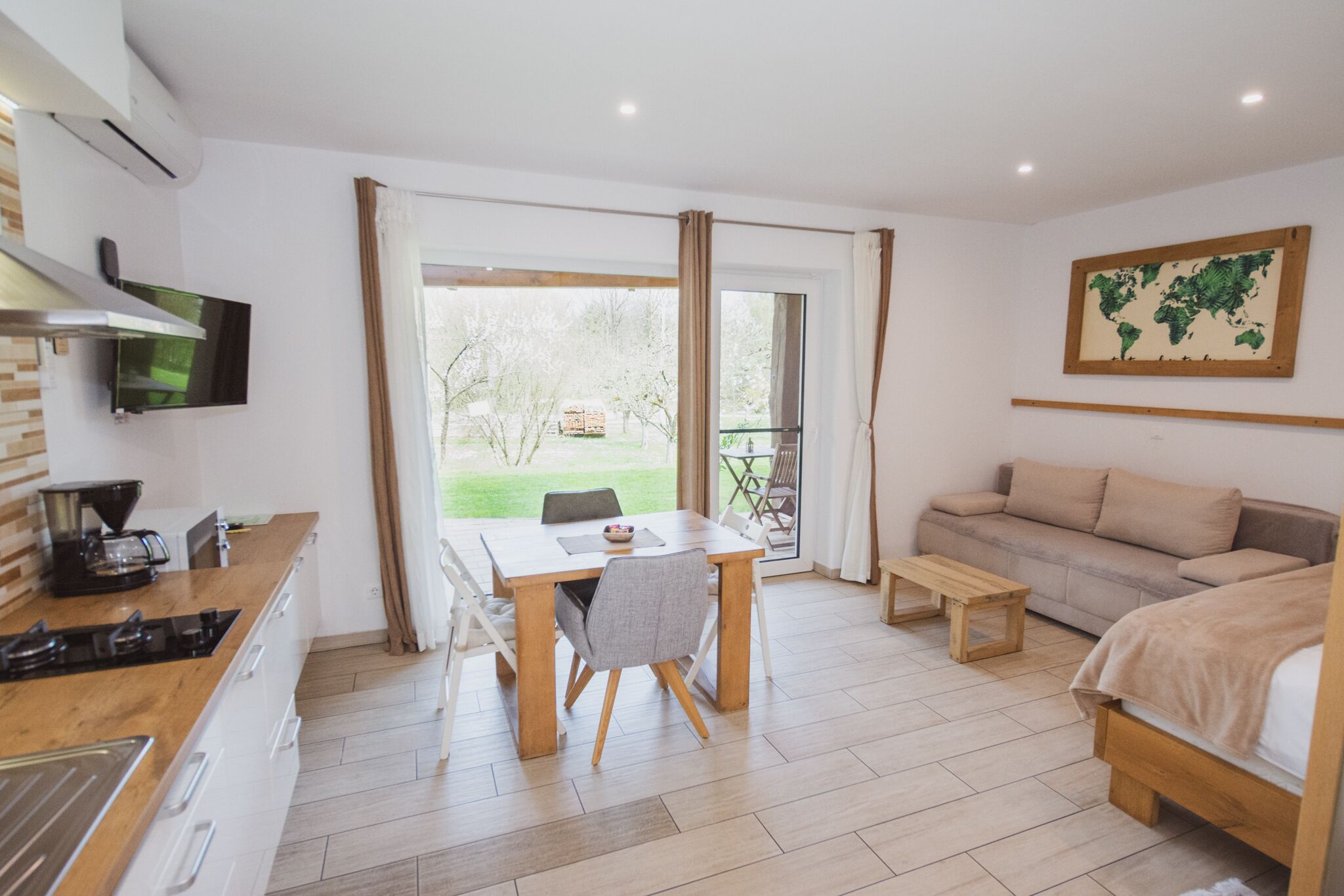 A modern, well-lit room with a kitchen area, a dining table with chairs, a sofa, and a bed.