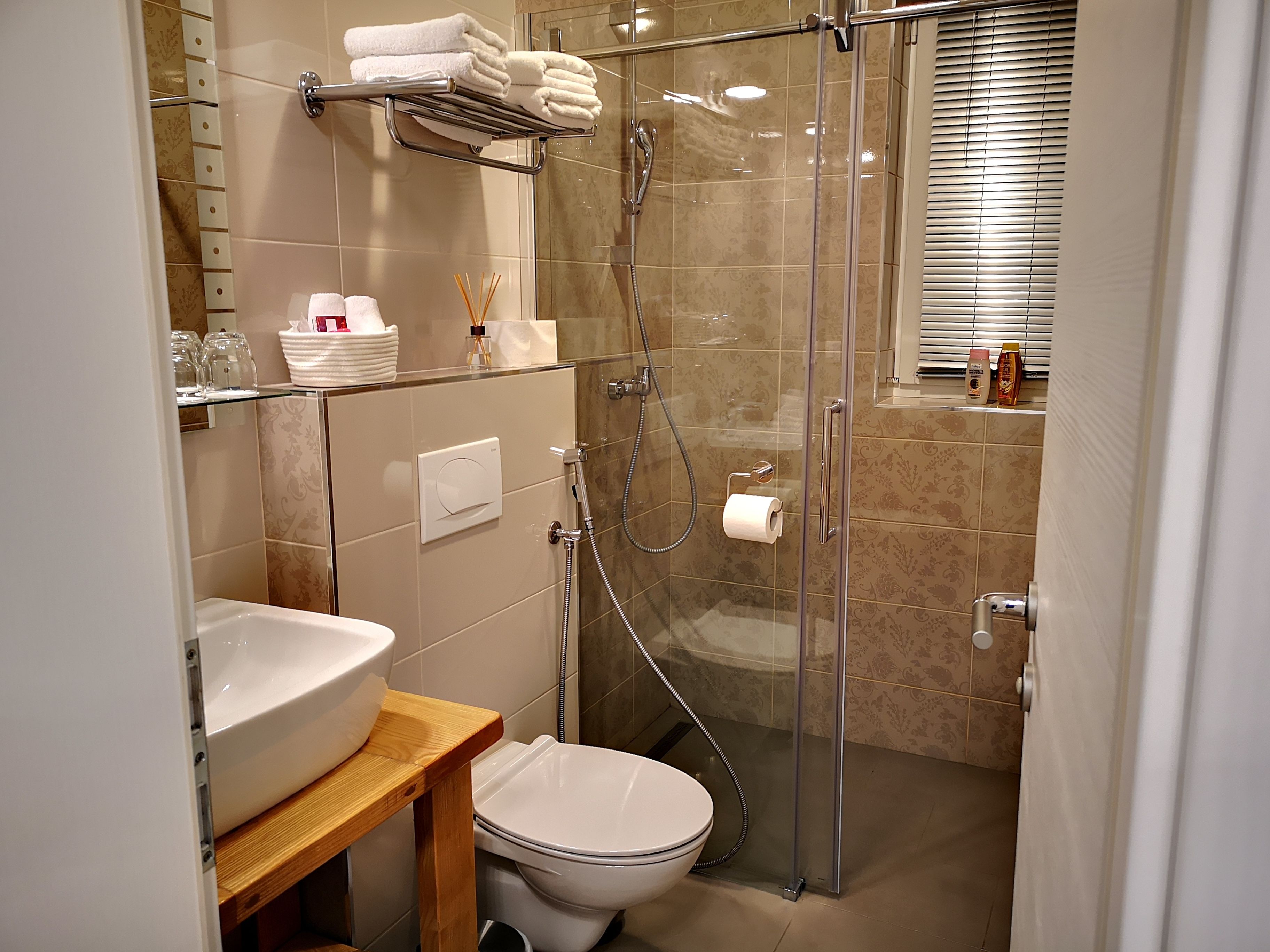 A modern bathroom with a glass-enclosed shower, a toilet, a sink, and a shelf with toiletries.