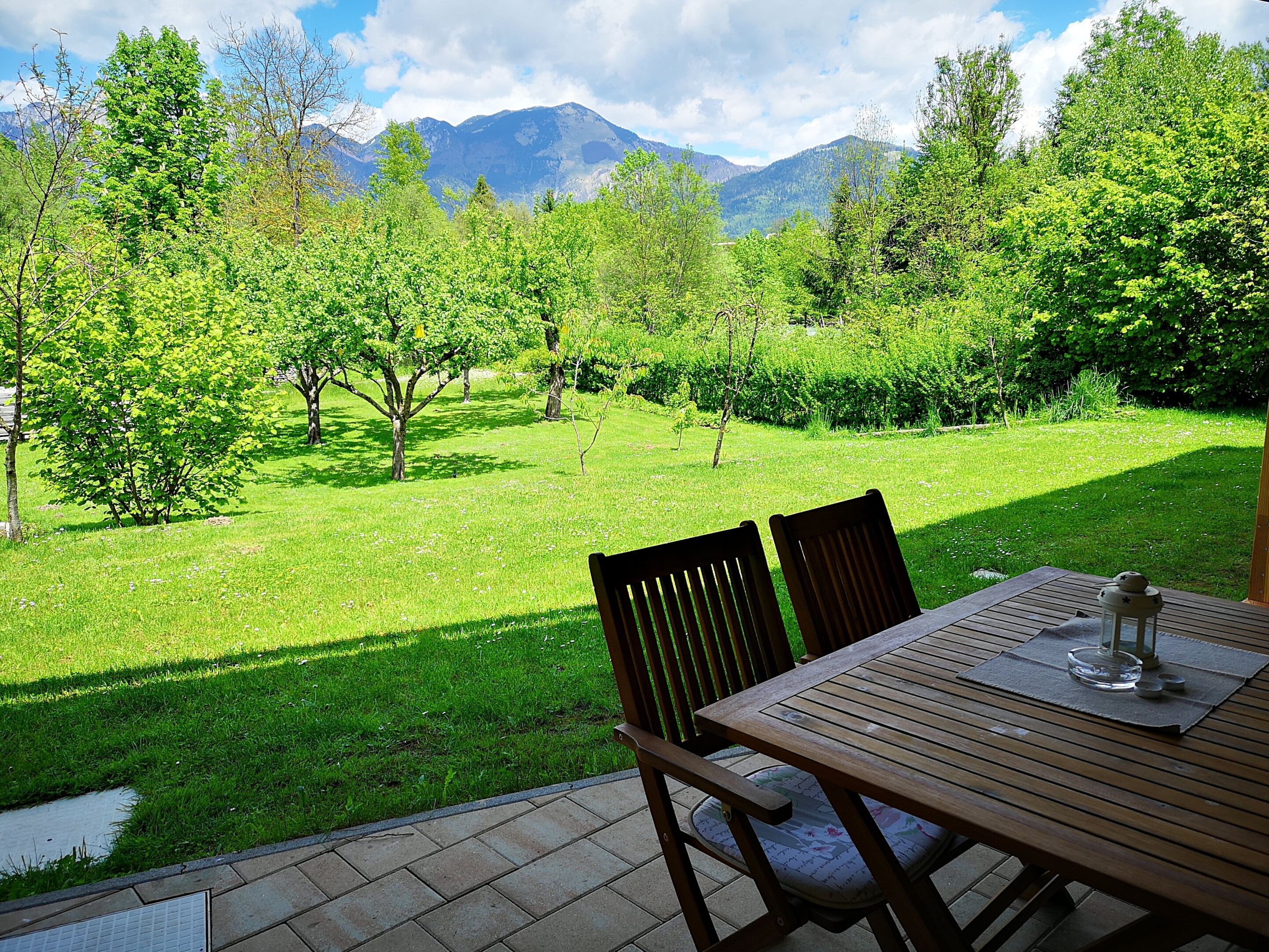 Un patio con mesa y sillas que da a un jardín exuberante y montañas.