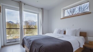 A bedroom with a large bed, a window with curtains, a bedside table, and a view of mountains.