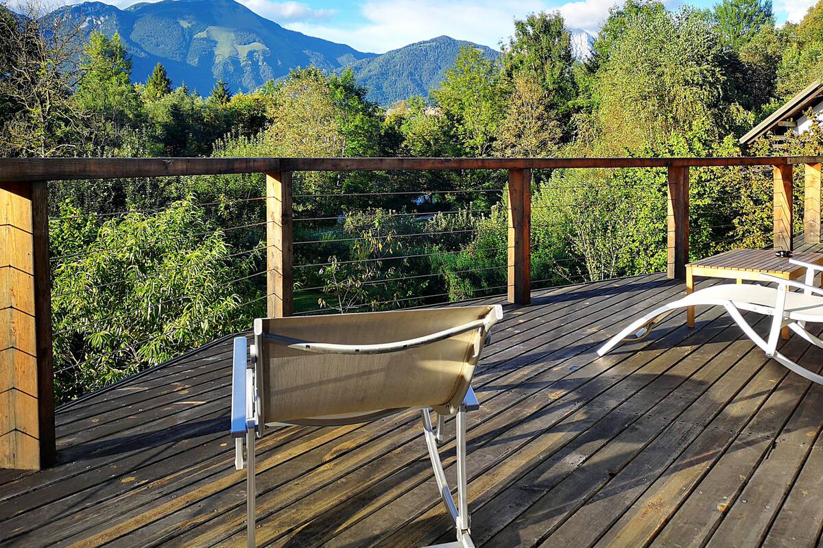 A wooden deck with a white rocking chair and a table, overlooking a mountainous landscape.