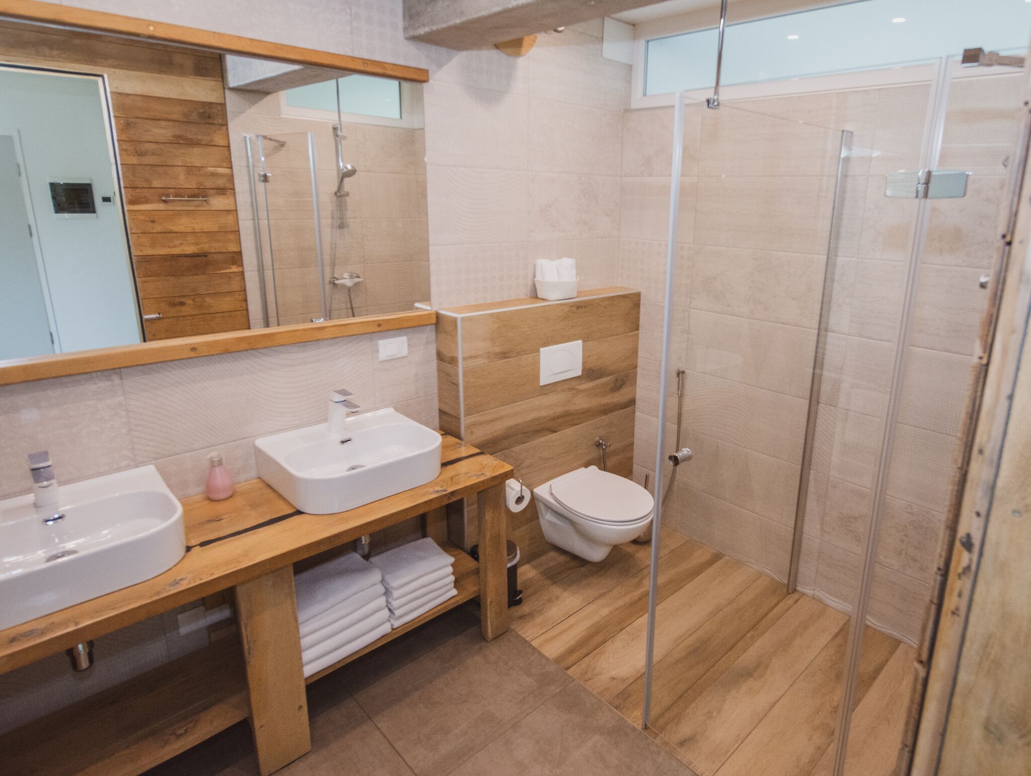 Um banheiro moderno com duas pias, vaso sanitário e chuveiro com box de vidro.