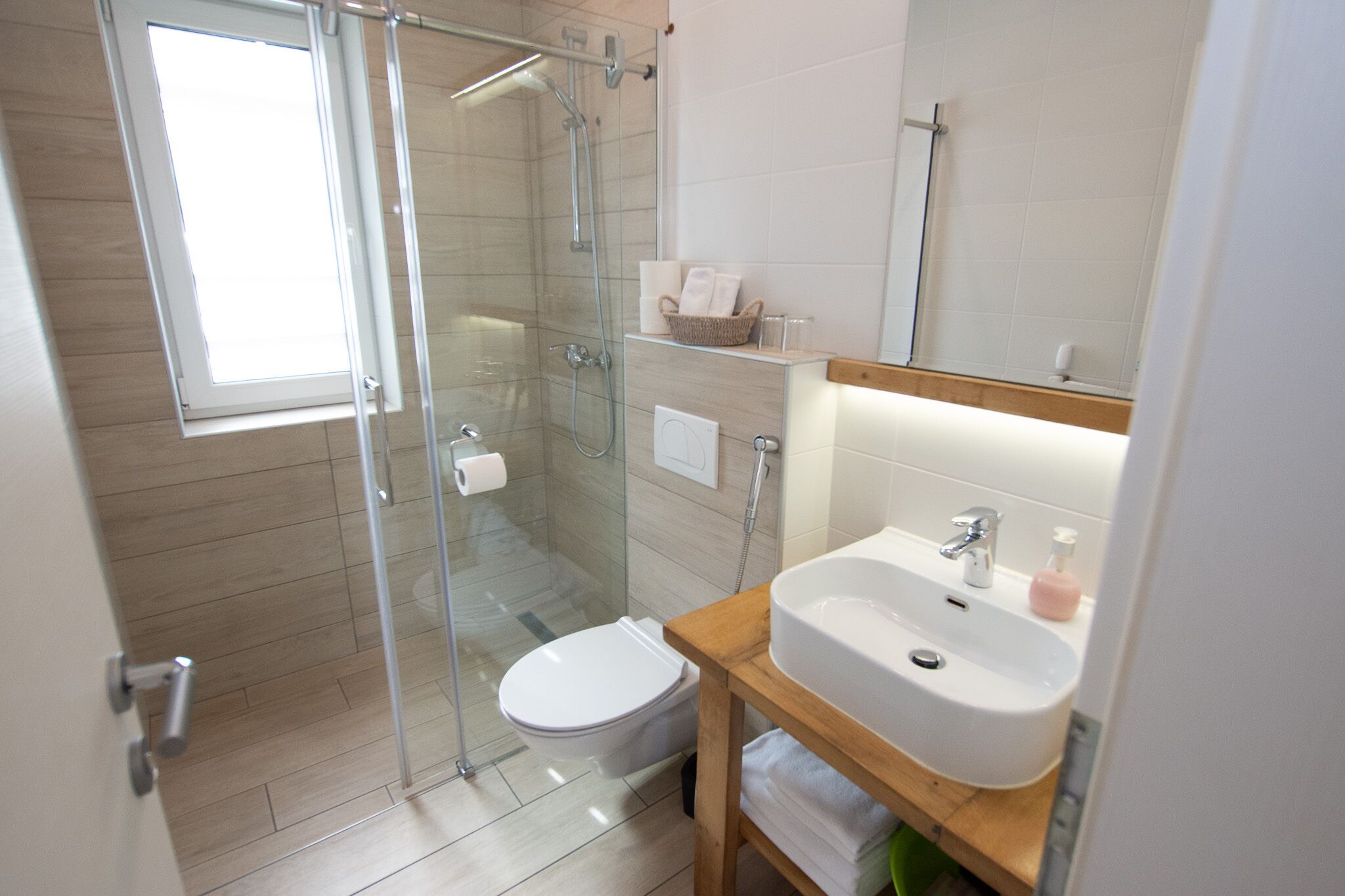 A modern bathroom with a glass-enclosed shower, a white toilet, and a wooden vanity with a sink.