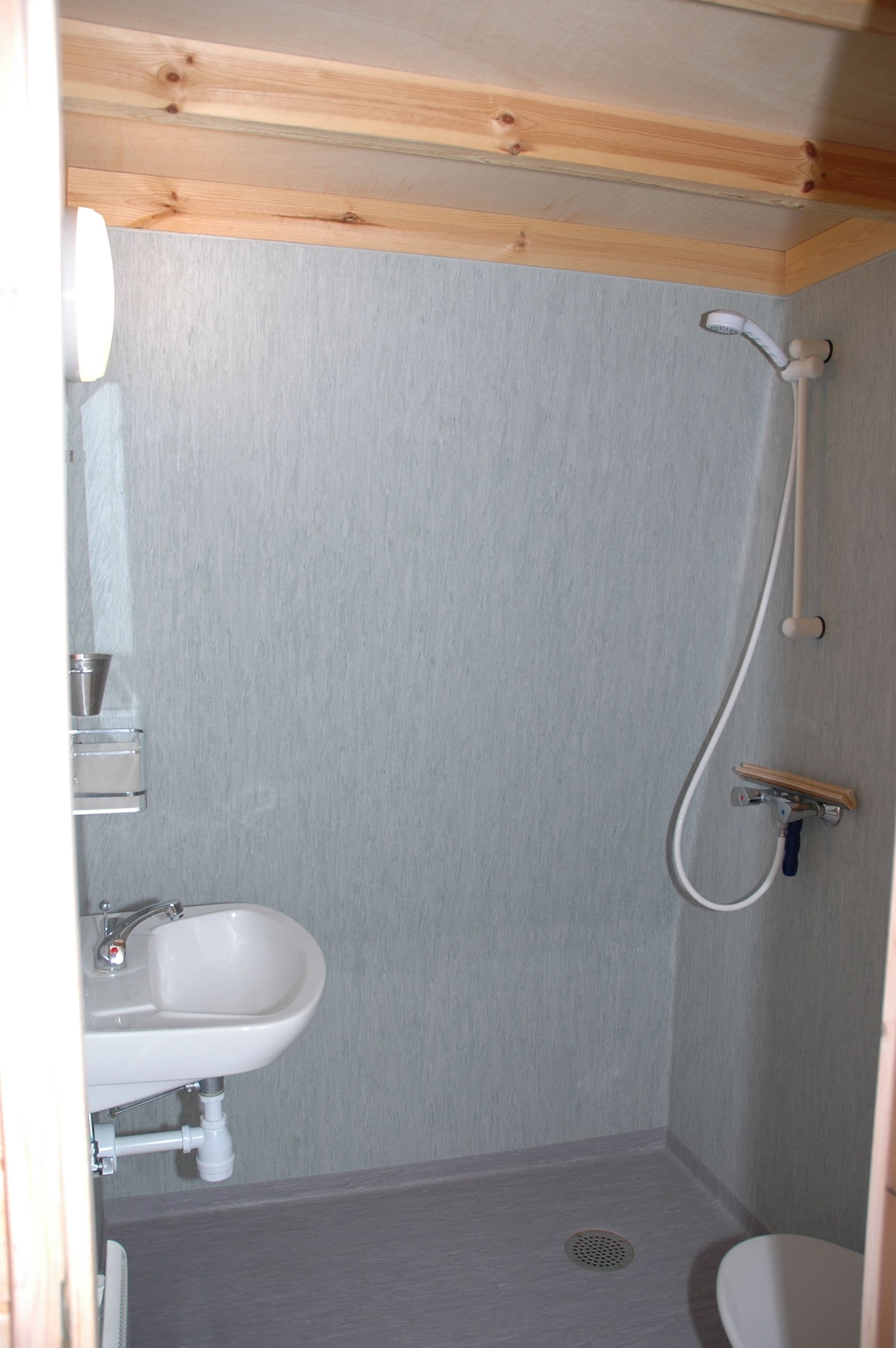 Une petite salle de bain avec un plafond en bois, un lavabo blanc et une douche.