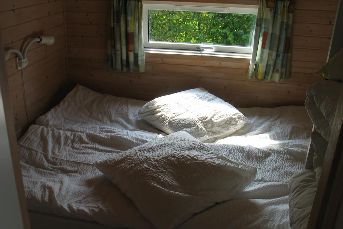 A small, cozy room with a single bed, a window with curtains, and a wooden wall.