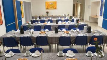 Un salón de conferencias con mesas redondas, sillas azules y manteles blancos.