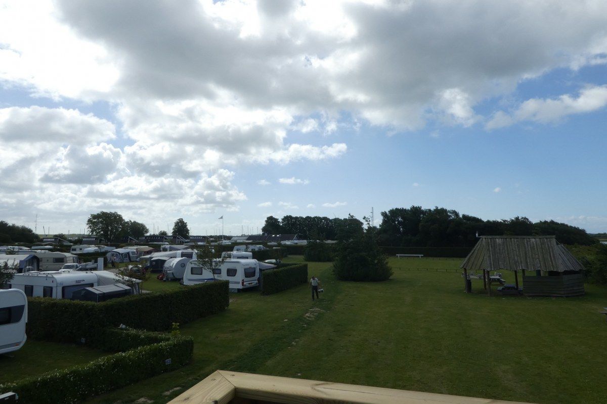 A campsite with RVs parked on a grassy area, a wooden structure, and a clear sky.