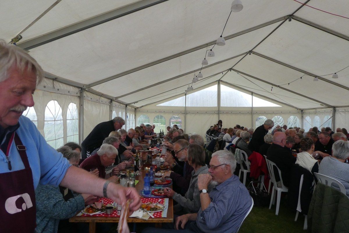 A large tent with tables and chairs, people seated and eating, and a person serving food.