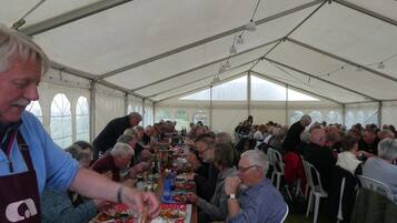 A large tent with tables and chairs, people seated and eating, and a person serving food.