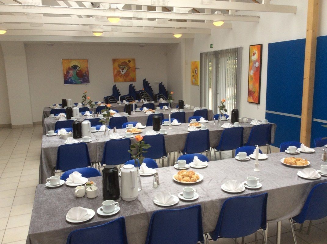 Un salón de conferencias con varias mesas dispuestas para una reunión, equipado con sillas, mesas y diversos elementos para comidas.
