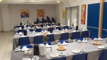 Un salón de conferencias con varias mesas dispuestas para una reunión, equipado con sillas, mesas y diversos elementos para comidas.