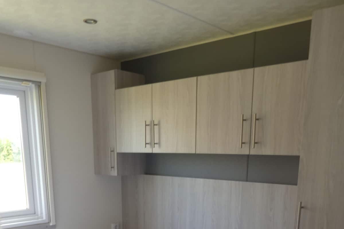 A bedroom with a bed, wooden cabinets, and a window.
