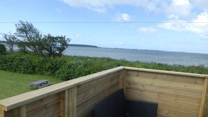 Una terraza de madera con una silla de mimbre y una mesa de picnic, con vista a un cuerpo de agua.
