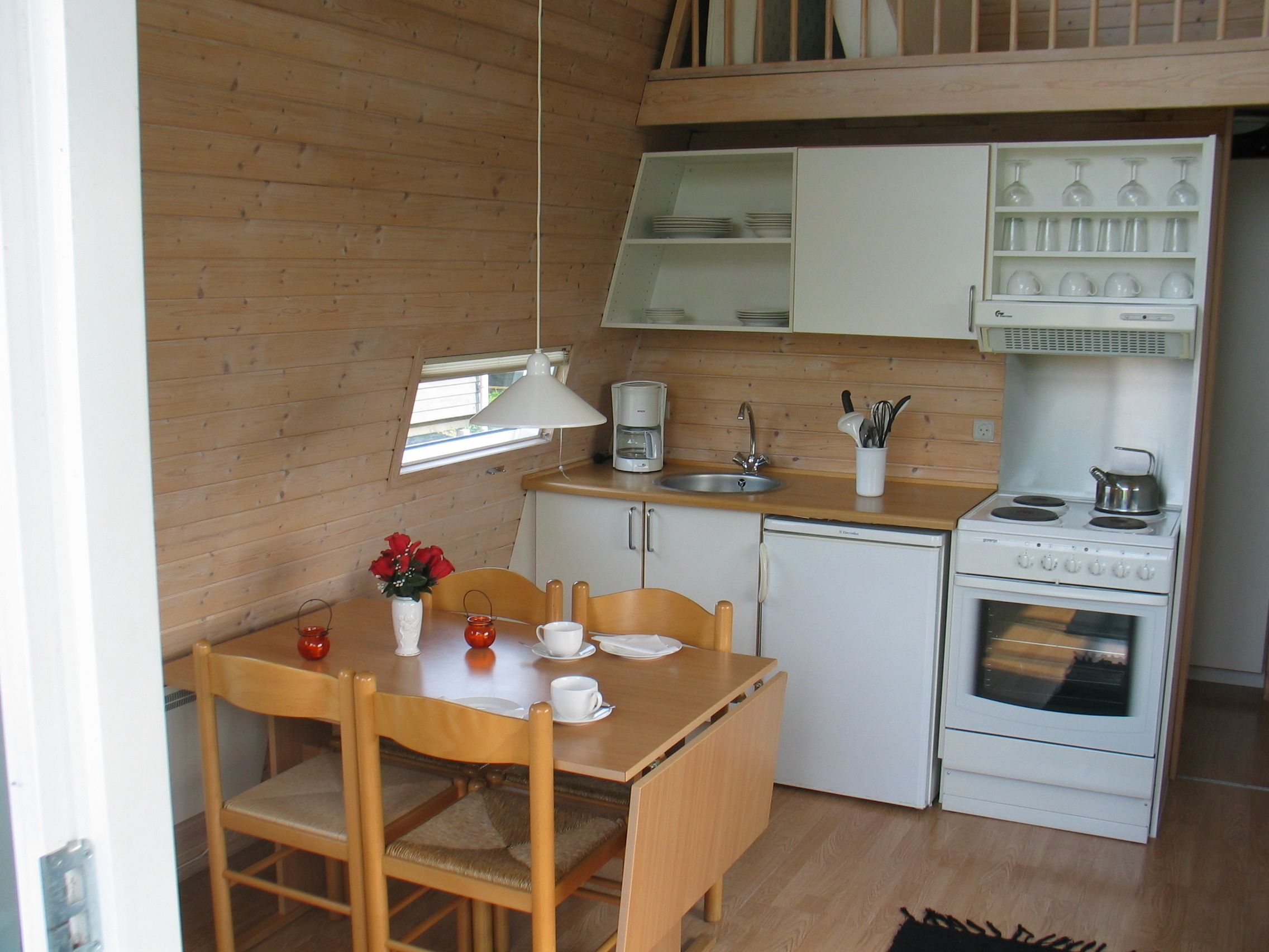 Eine kleine Küche mit Holzausstattung, Spüle, Herd und einem Essbereich mit Stühlen und Tisch.