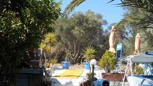 A garden pathway leading to a seating area with umbrellas and potted plants. - Meltemia Studios Samos (Samos)