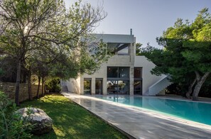 A modern house with a swimming pool, a stone wall, and trees. - Minimal Blue Villa (Markopoulo Mesogaias)