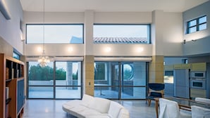 A spacious living area with a white sofa, a dining table with chairs, and a kitchen with built-in appliances. - Minimal Blue Villa (Markopoulo Mesogaias)