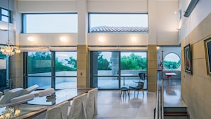A spacious interior with a high ceiling, large windows, and a modern staircase. - Minimal Blue Villa (Markopoulo Mesogaias)