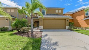 A two-story house with a garage, a well-maintained lawn, and a palm tree. - 4 bed House/w pool & Garage (Kissimmee)
