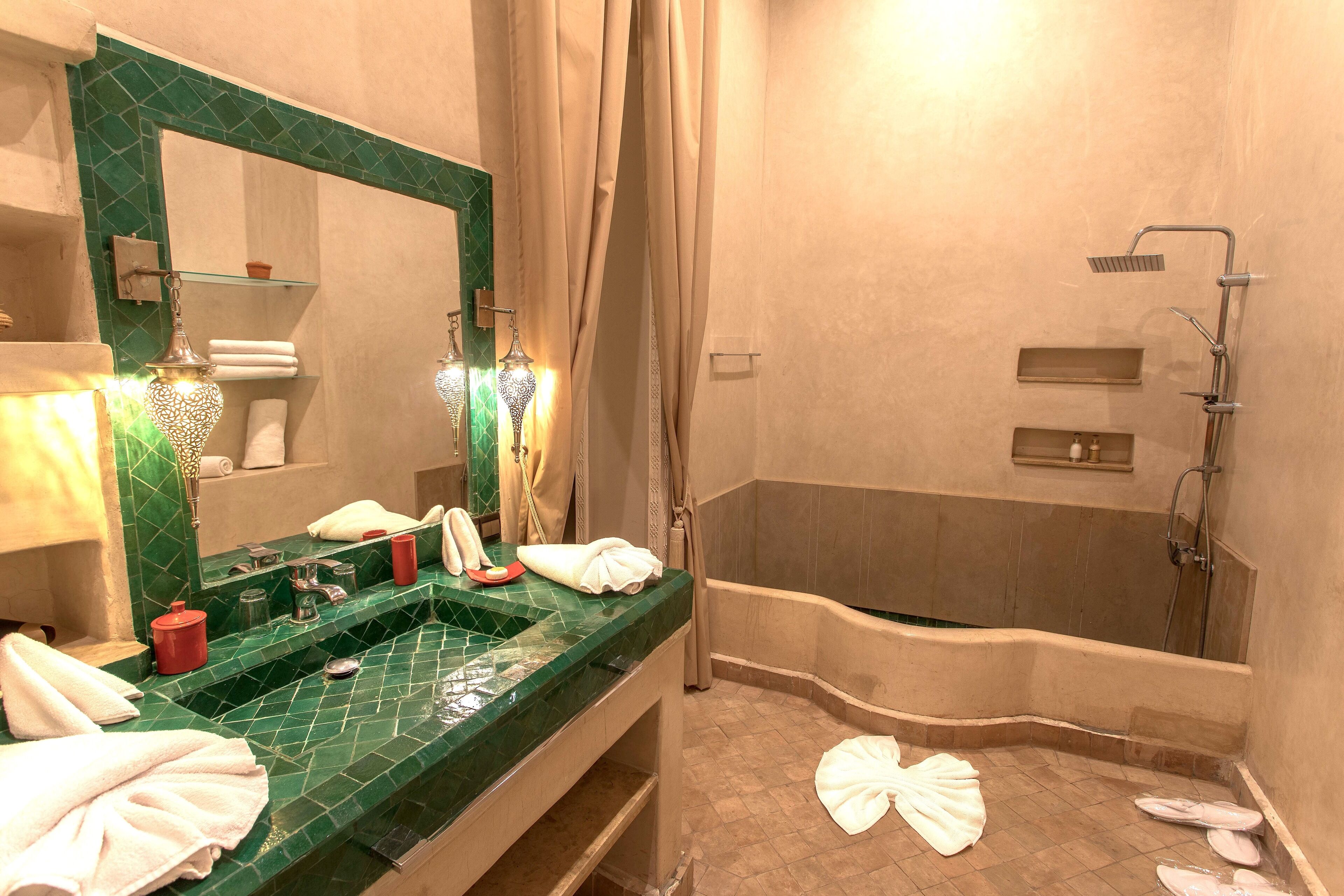 Une salle de bain avec un lavabo aux carreaux verts, un grand miroir, une baignoire et une douche.