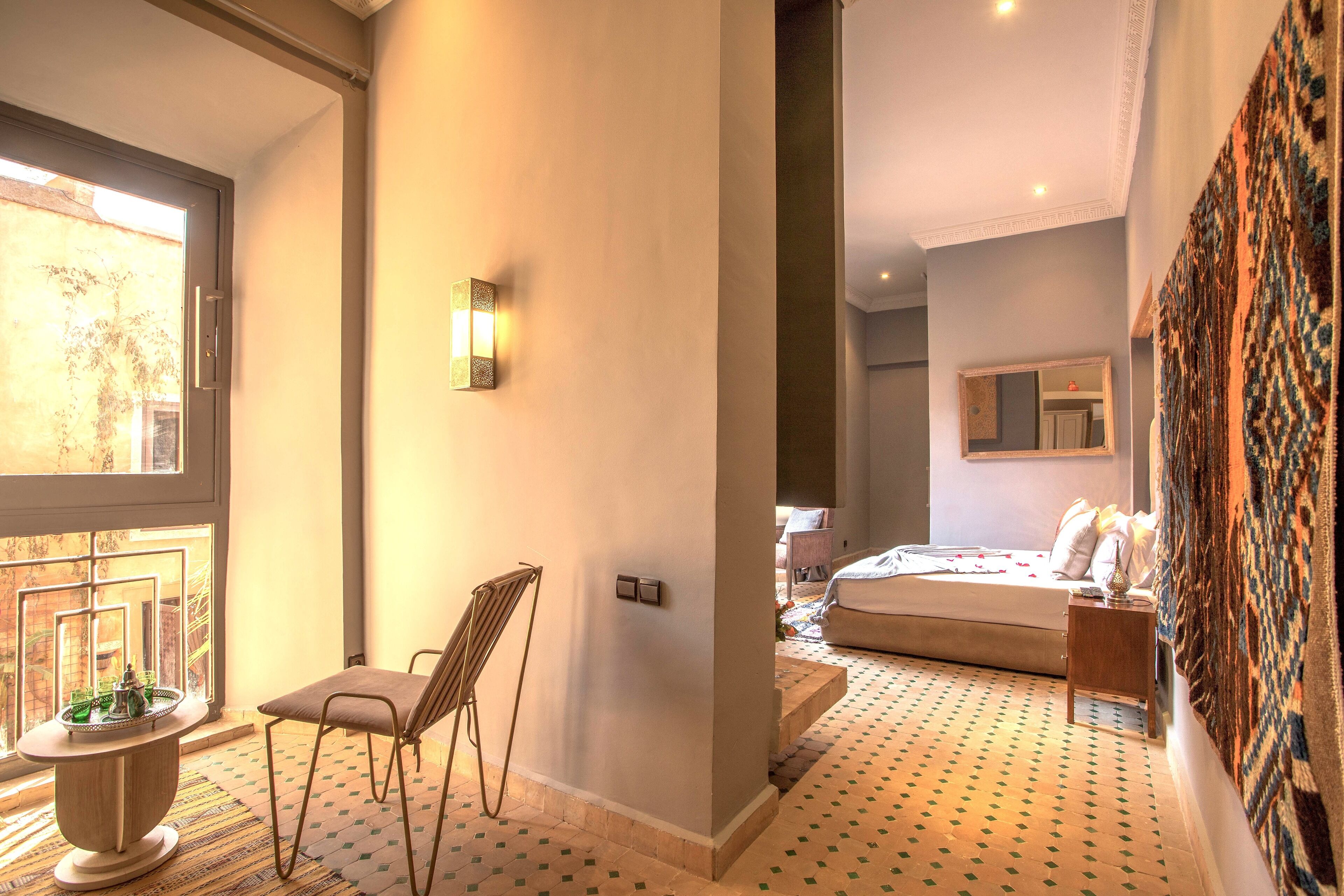 A bedroom with a bed, a chair, a small table, and a wall-mounted light fixture.