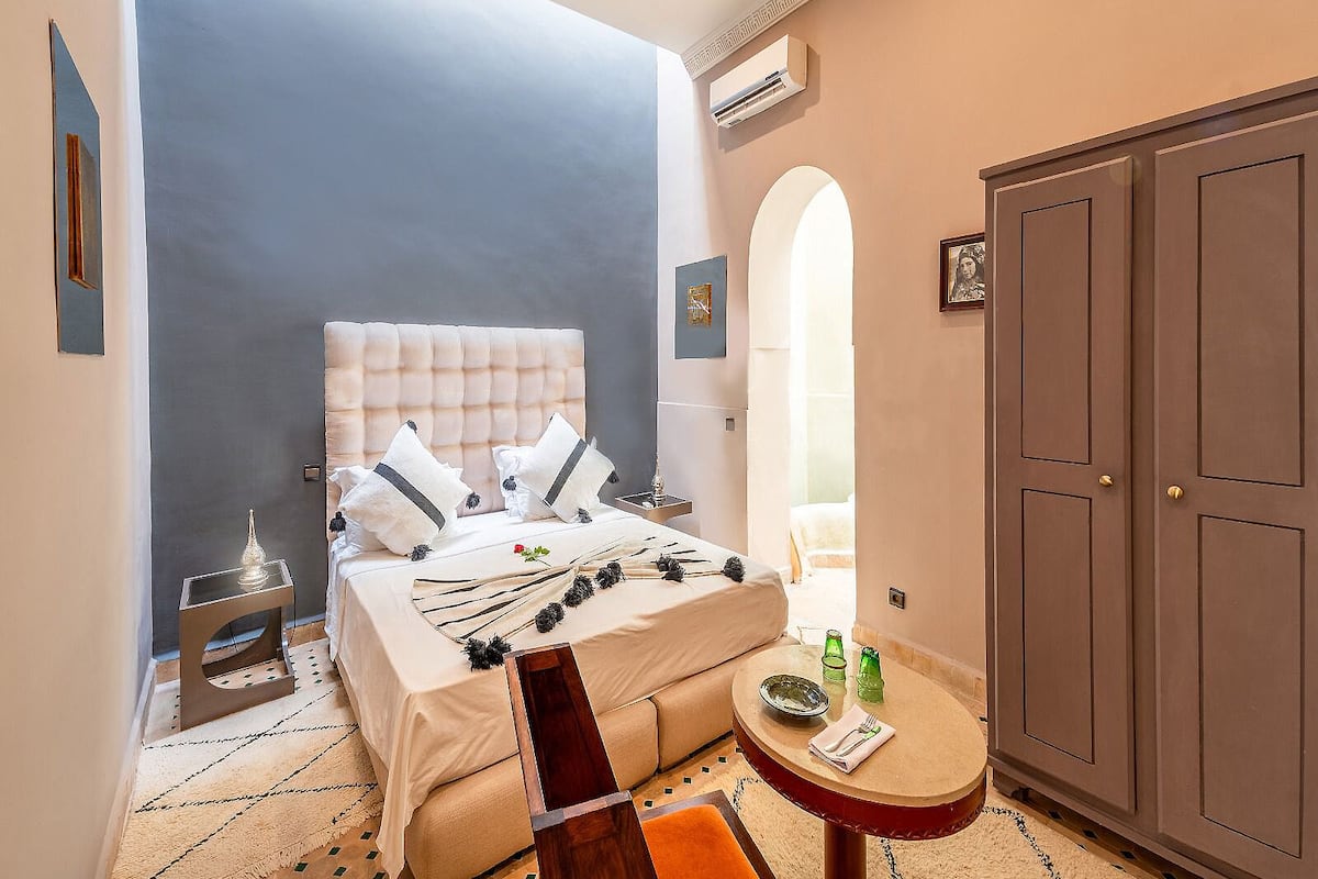 A bedroom with a bed, bedside table, wardrobe, and a small round table with a plate and utensils.