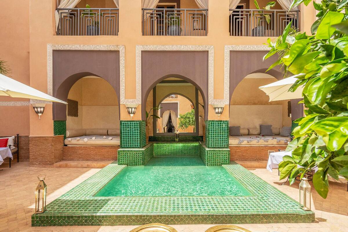 A courtyard with a pool, seating areas, and a building with arches and balconies.