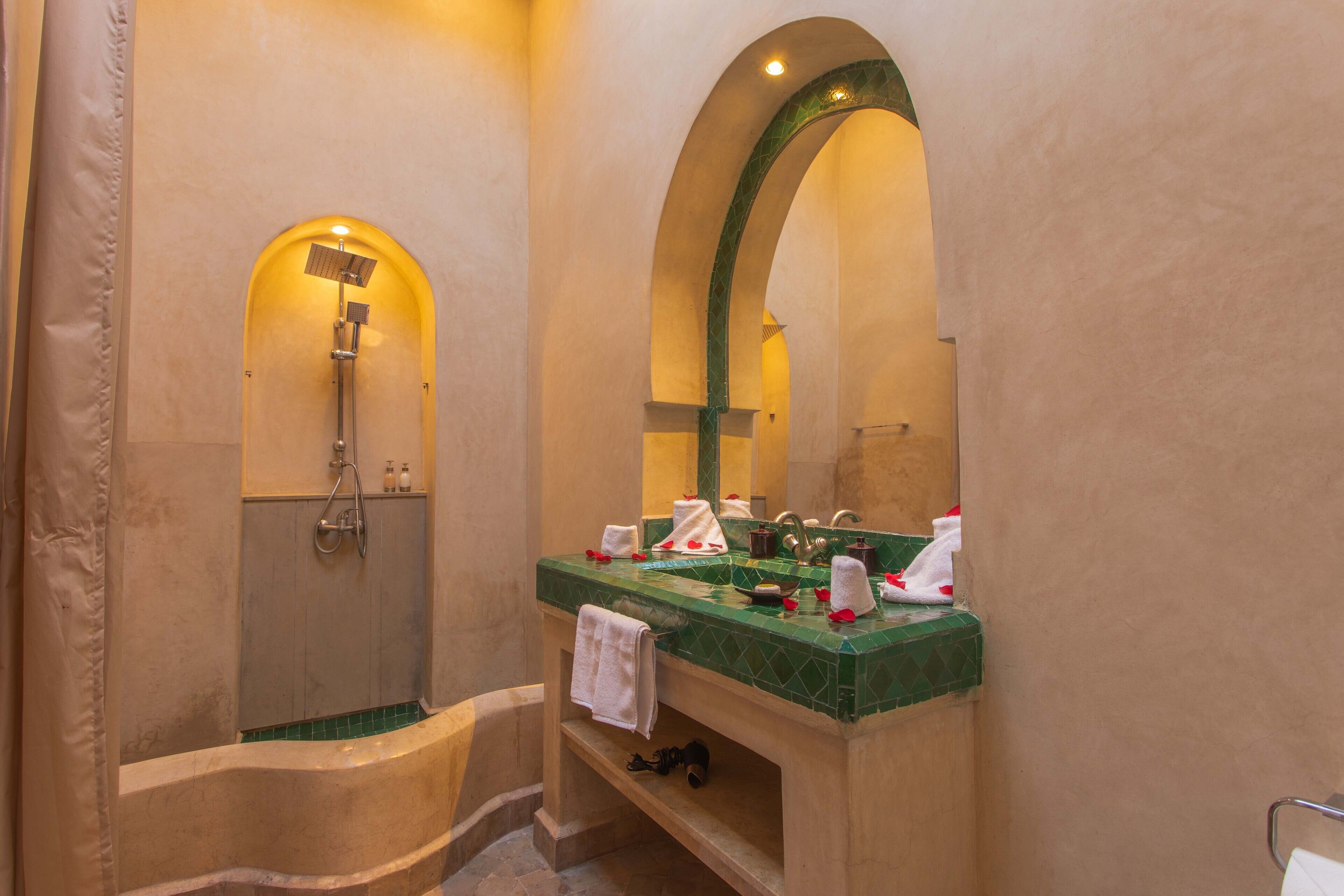 A bathroom with a bathtub, a shower, a sink with a green countertop, and a mirror with an arched frame.