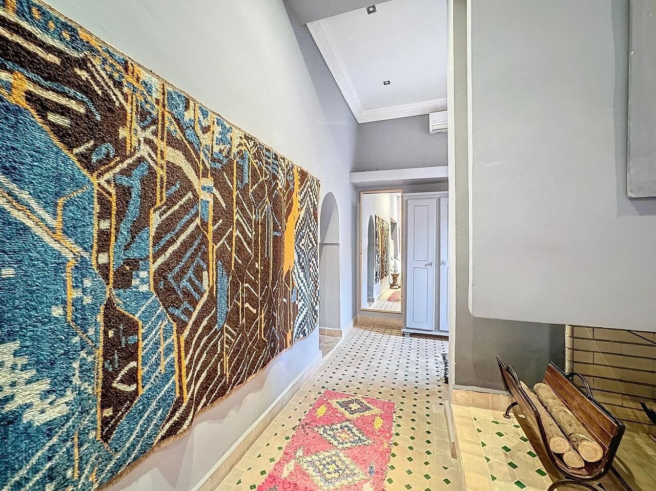 A hallway with patterned rugs, a bench, and a door leading to another room.