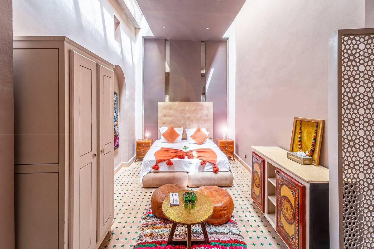 A narrow hallway leading to a bedroom with a large bed, a small round table, and a cabinet.