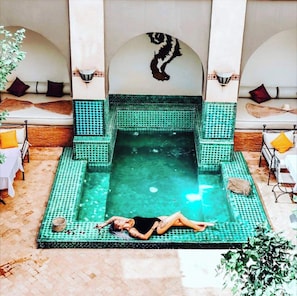 A pool area with a person lying on a mat, surrounded by tiled walls and benches. - Le Medina Privilége Riad & Spa (Marrakech)