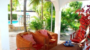 A covered outdoor seating area with wicker furniture and a view of a pool and tropical vegetation. - Paradera Paradise (Paradera)