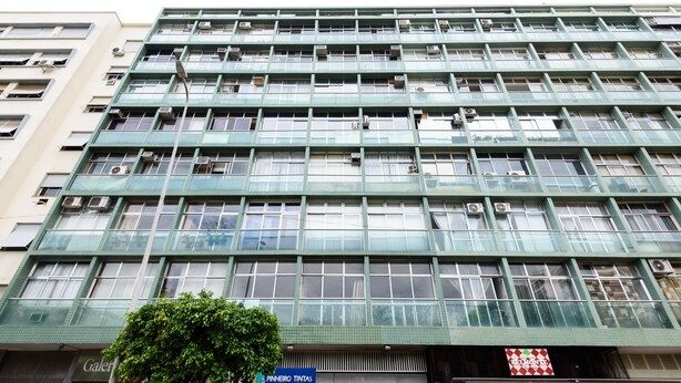 Um edifício moderno de vários andares, com projeto arquitetônico que destaca uma grade de janelas e aparelhos de ar condicionado.