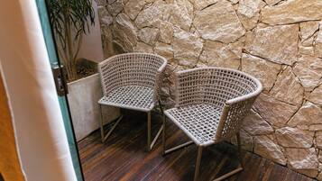 Two wicker chairs with metal legs, positioned against a stone wall, on a wooden floor.